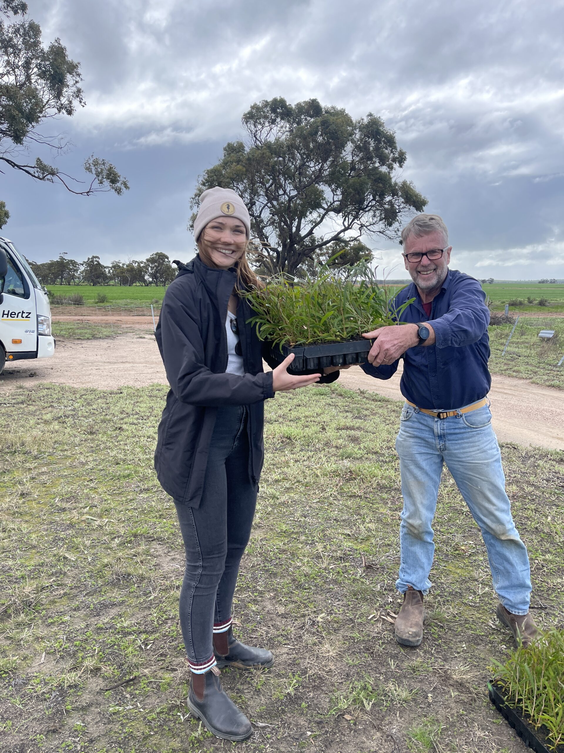 Man and a woman holding a tray of seedlings in a field
