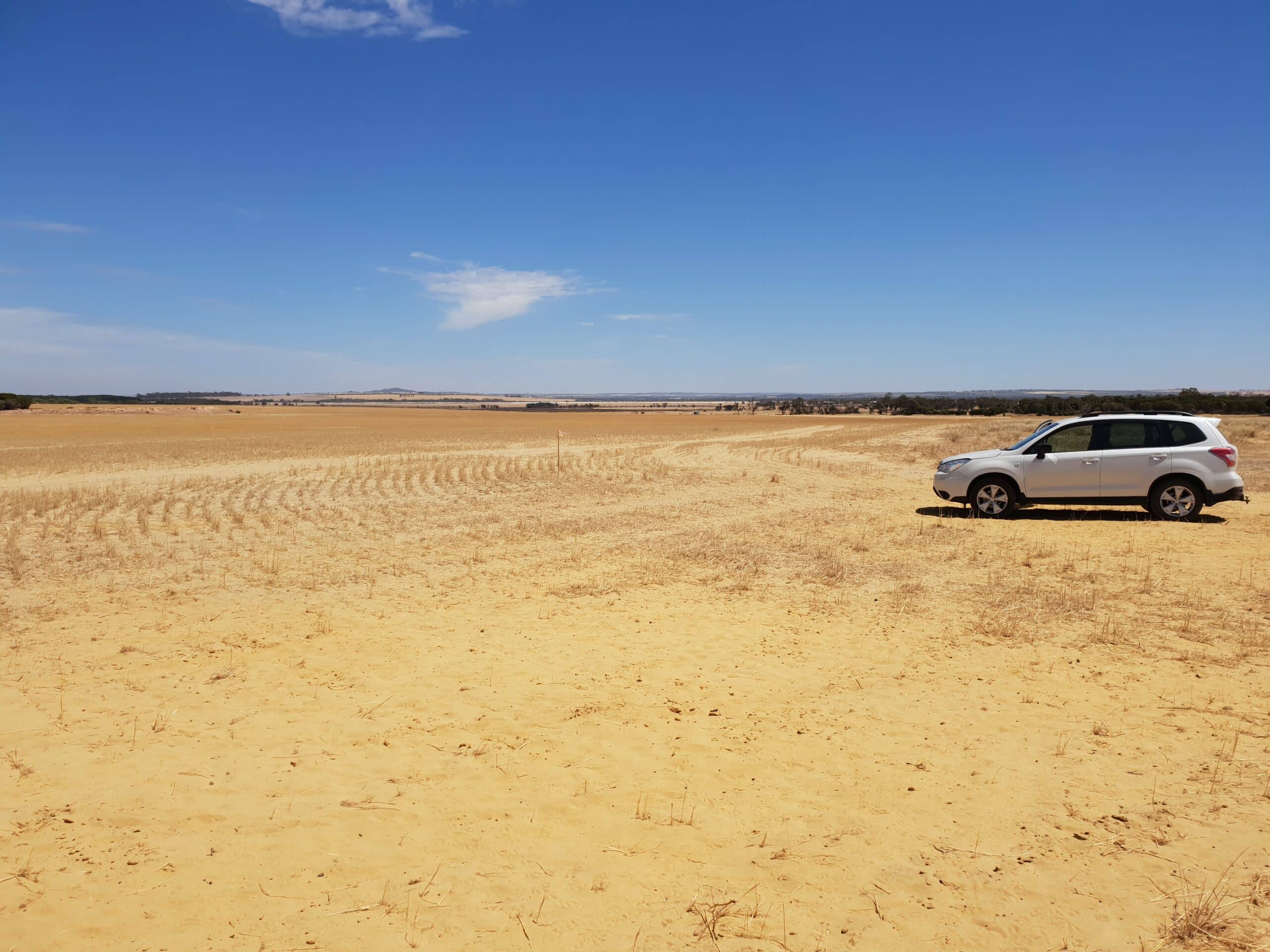 Cleared area of flat land with sandy yellow soil and silver car