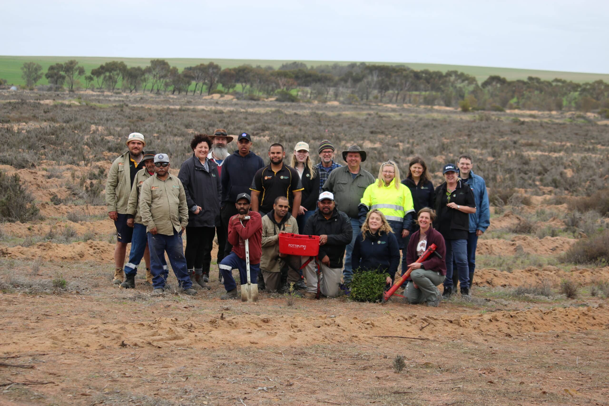 Group photo of 19 people with seedlings buckets standing in a cleared area