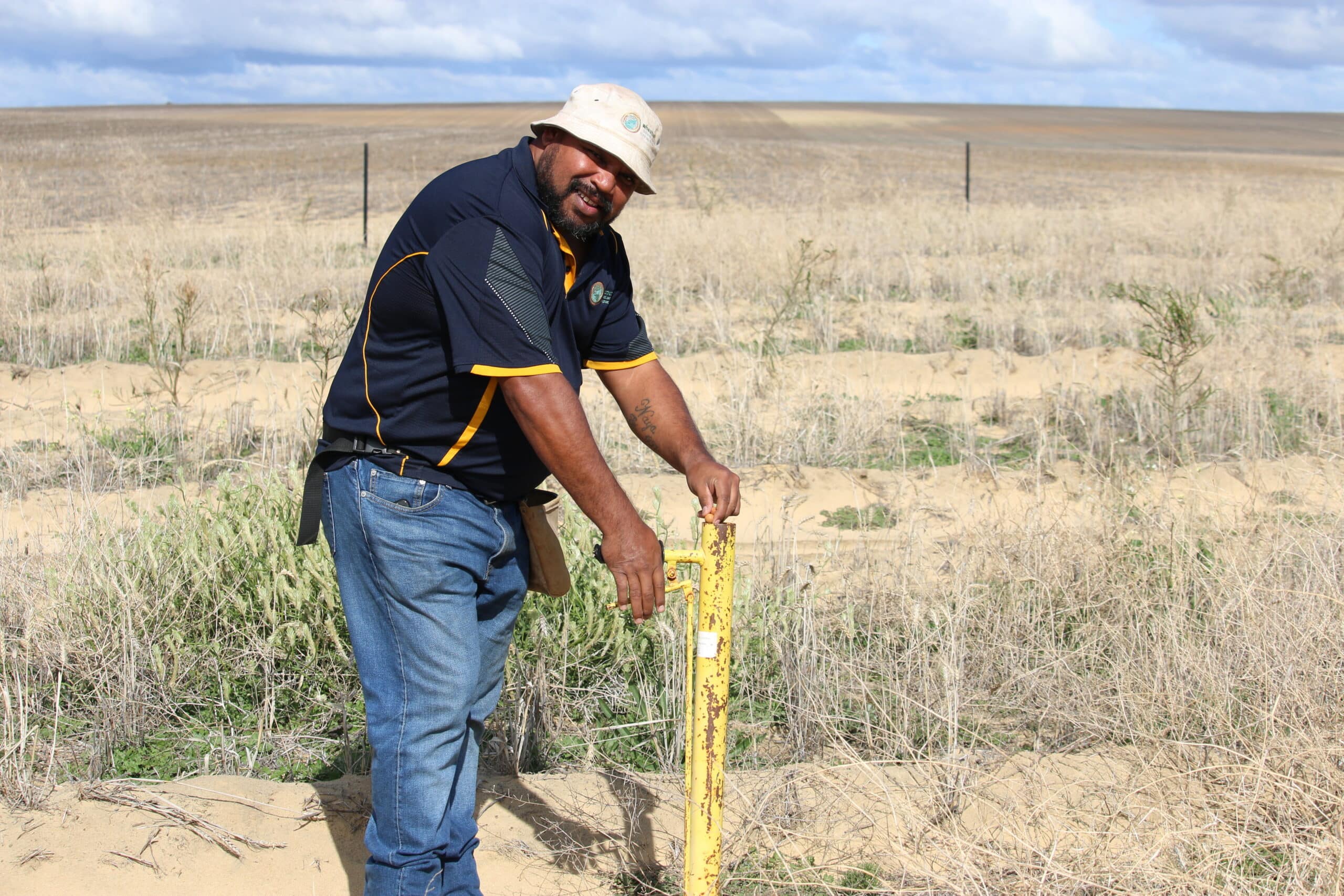 Man smiling whilst planting a seedling into a planting row with a pottiputki