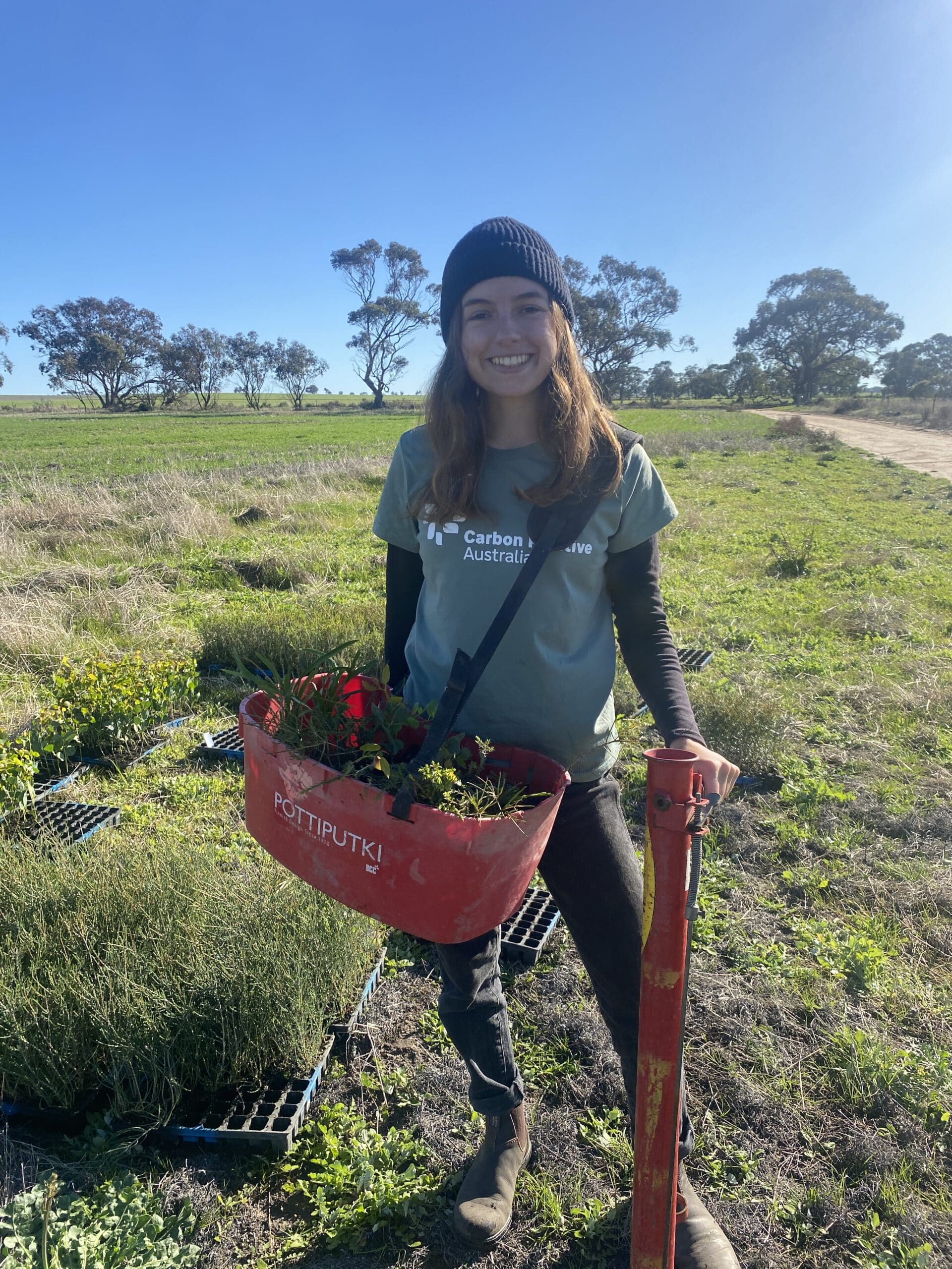 Woman posing with a bucket full of seedlings and a pottiputki