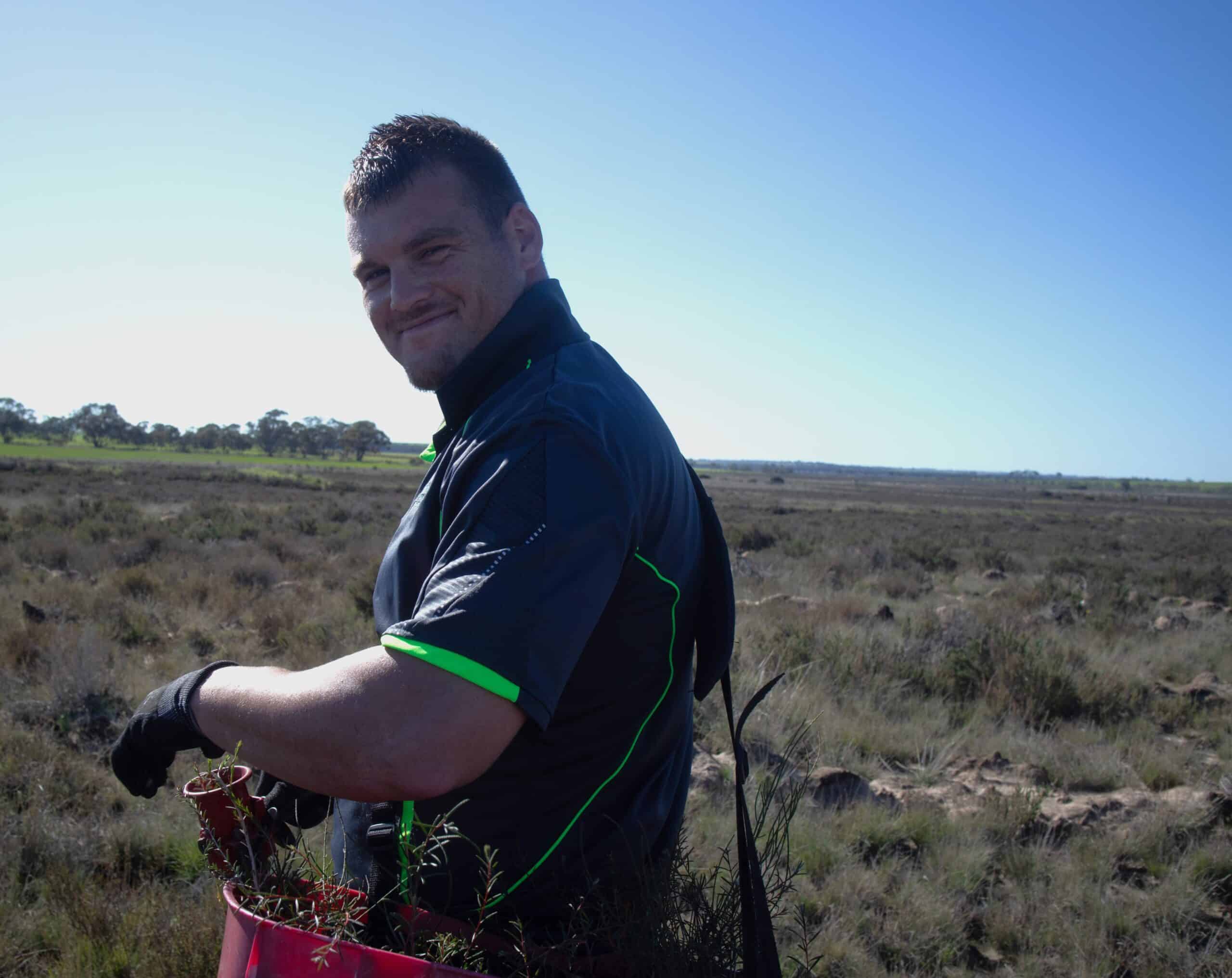 Mid shot of a man smiling with a bucket of seedlings