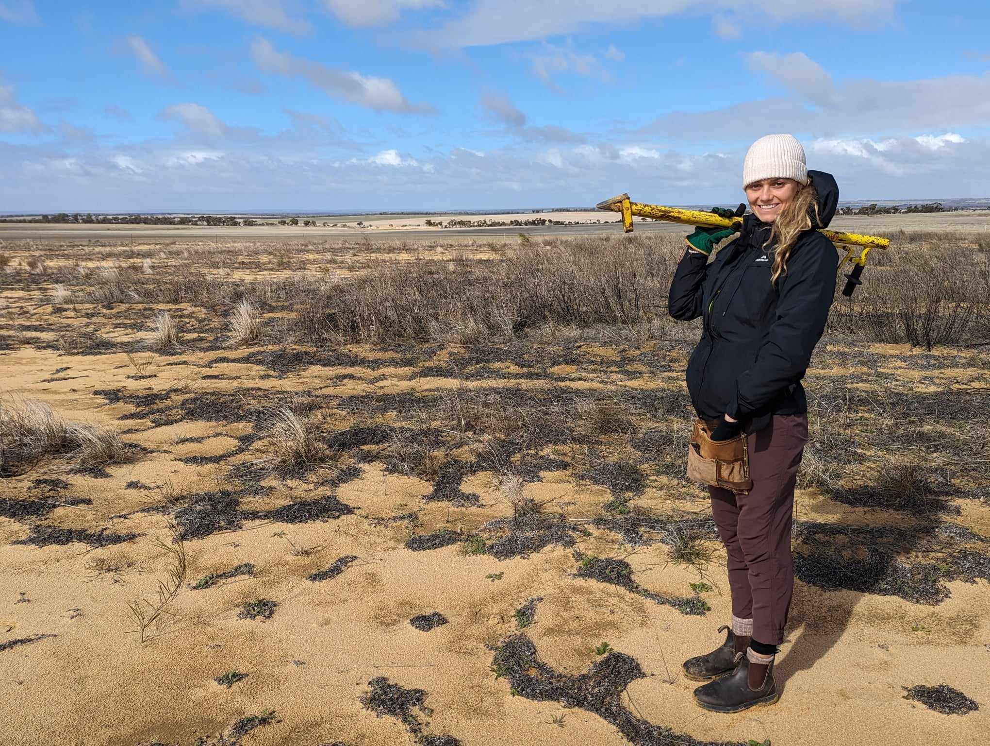 Woman smiling for a photo standing on yellow soil with a pottiputki