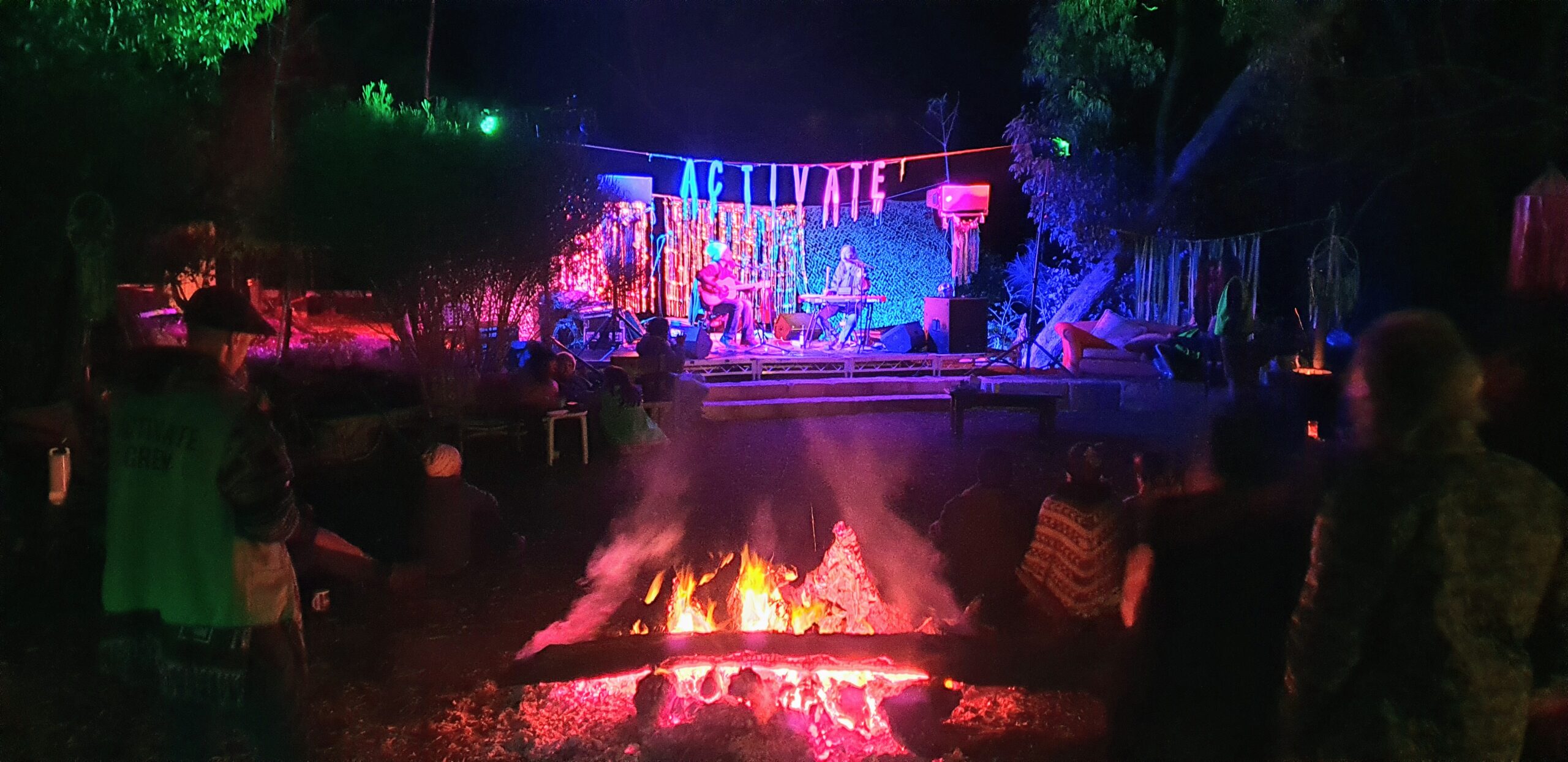 people sitting and standing a fire with musician on a stage in the background