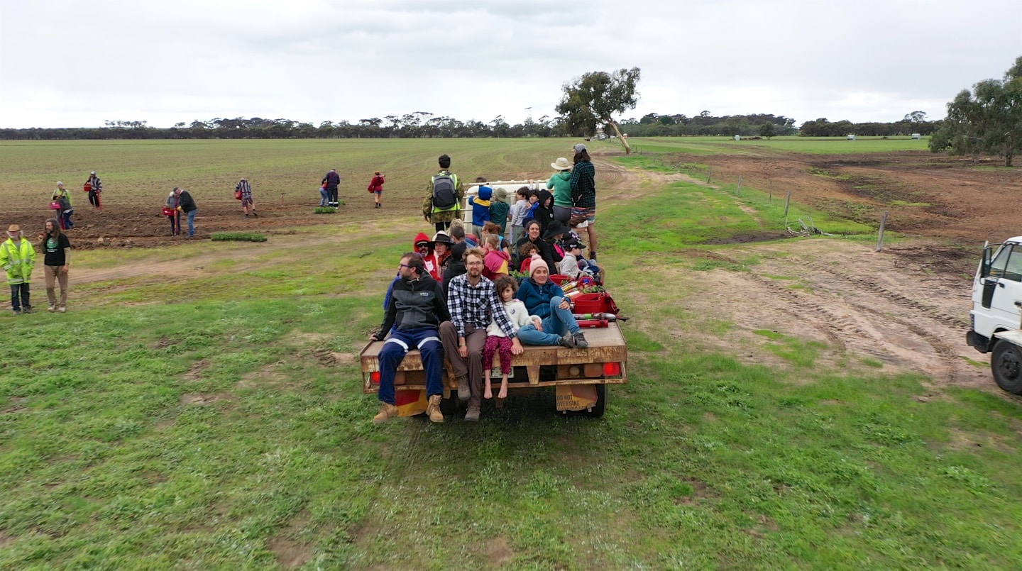 Children and Adults sitting on the back of a cart tray in an open paddock