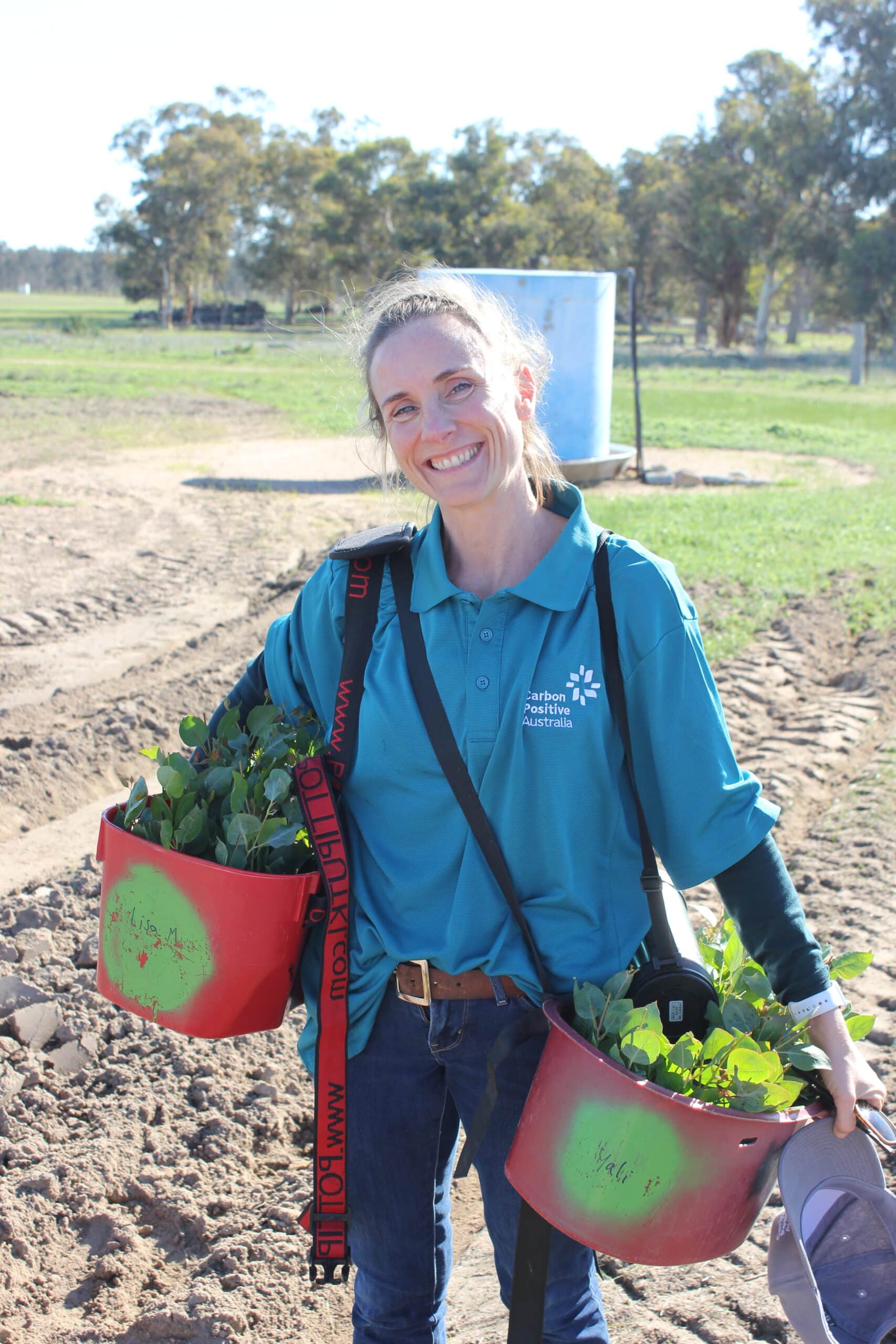 Women standing and smiling for a photo whilst holding two bucket full of seedlings