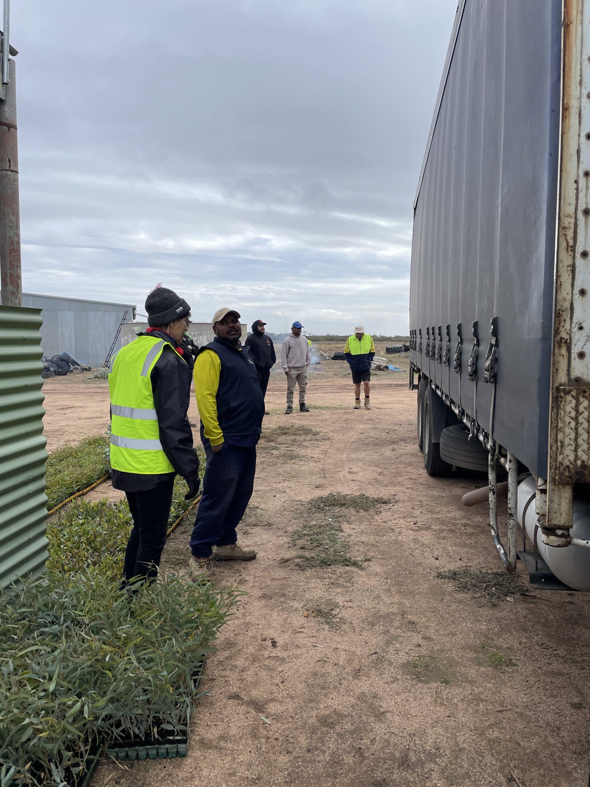 People standing next to the side of a truck with seedling trays behind them