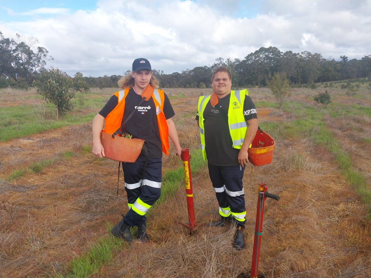 Two men standing with pottiputkis and seedling buckets.
