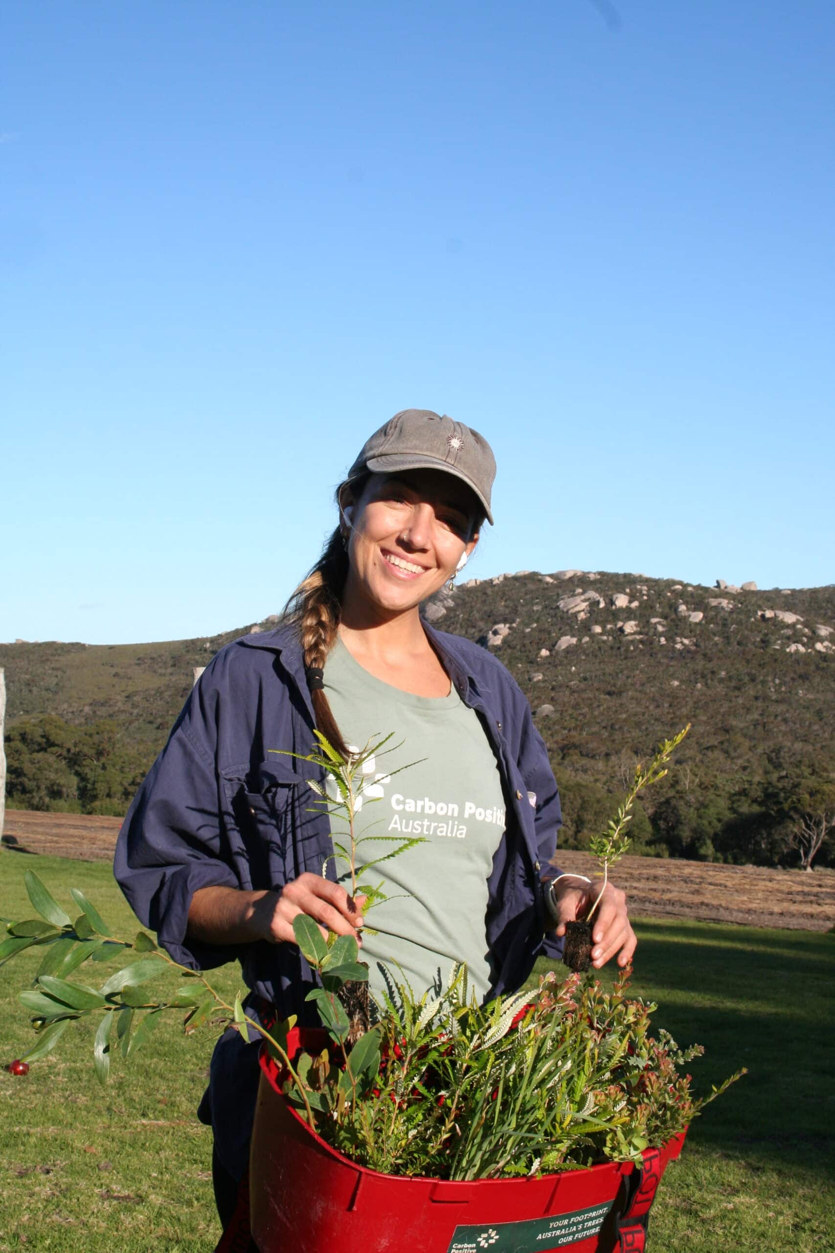 Woman with a full seedling bucket, holding a seedling in each hand.