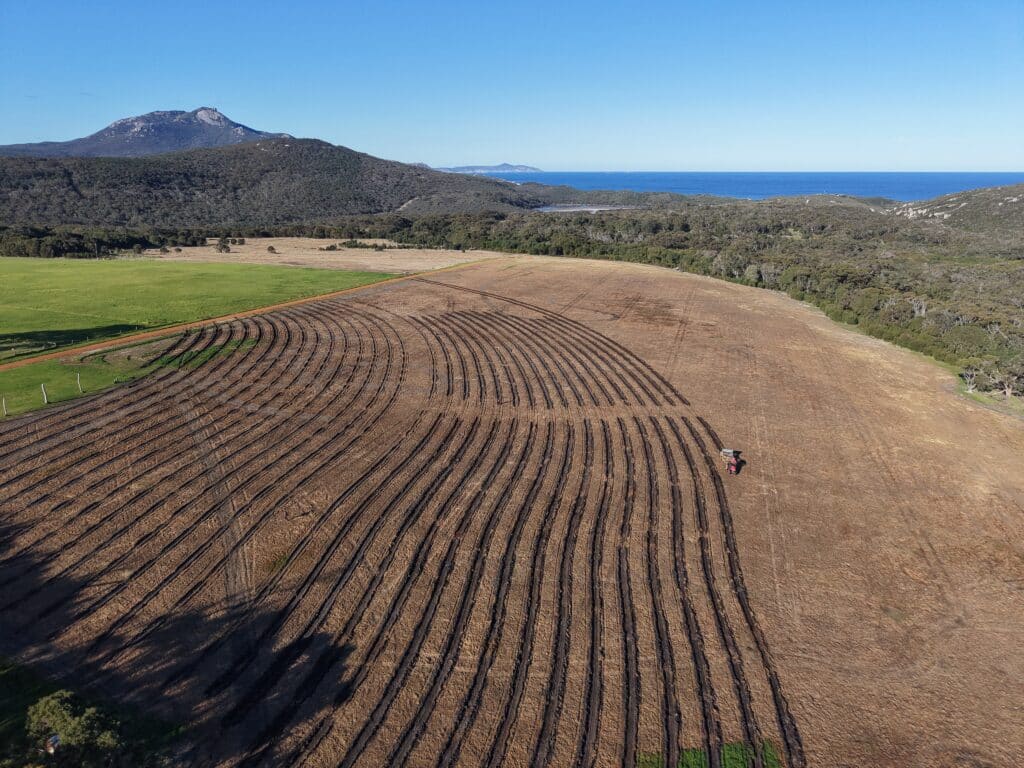 Drone image of tractor ripping planting lines with mountain in background.